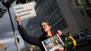A woman holds a placard that reads: “Hamas, sign the peace agreement!” while holding photographs of German citizens who are among the hostages still being held by Hamas in Gaza during a demonstration outside the Foreign Ministry on Oct. 2, 2025, in Berlin. 