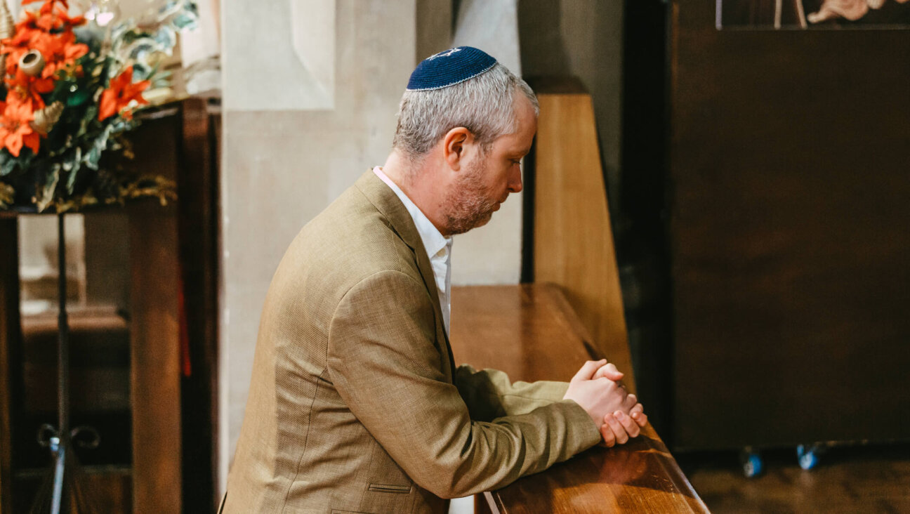 Portrait of a Jewish man kneeling and praying in the synagogue. The man is wearing a yarmulke on his head as he sits alone in the synagogue.