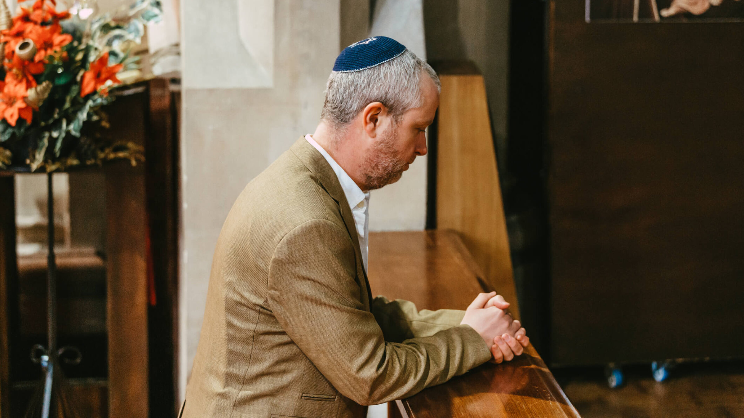 Portrait of a Jewish man kneeling and praying in the synagogue during Yom Kippur. The man is wearing a yarmulke on his head as he sits alone in the synagogue.