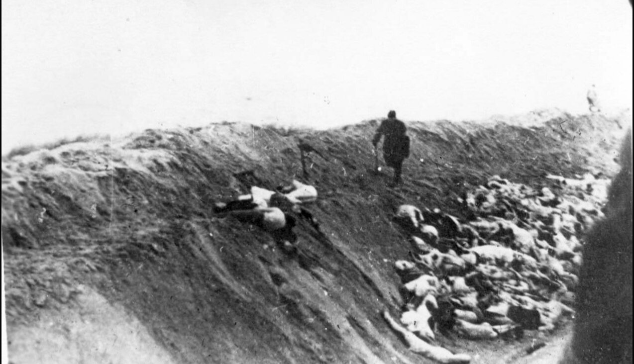 A Latvian collaborator kicks the bodies of Jewish women and children into a ditch after their execution, December 15, 1942 (Yad Vashem).