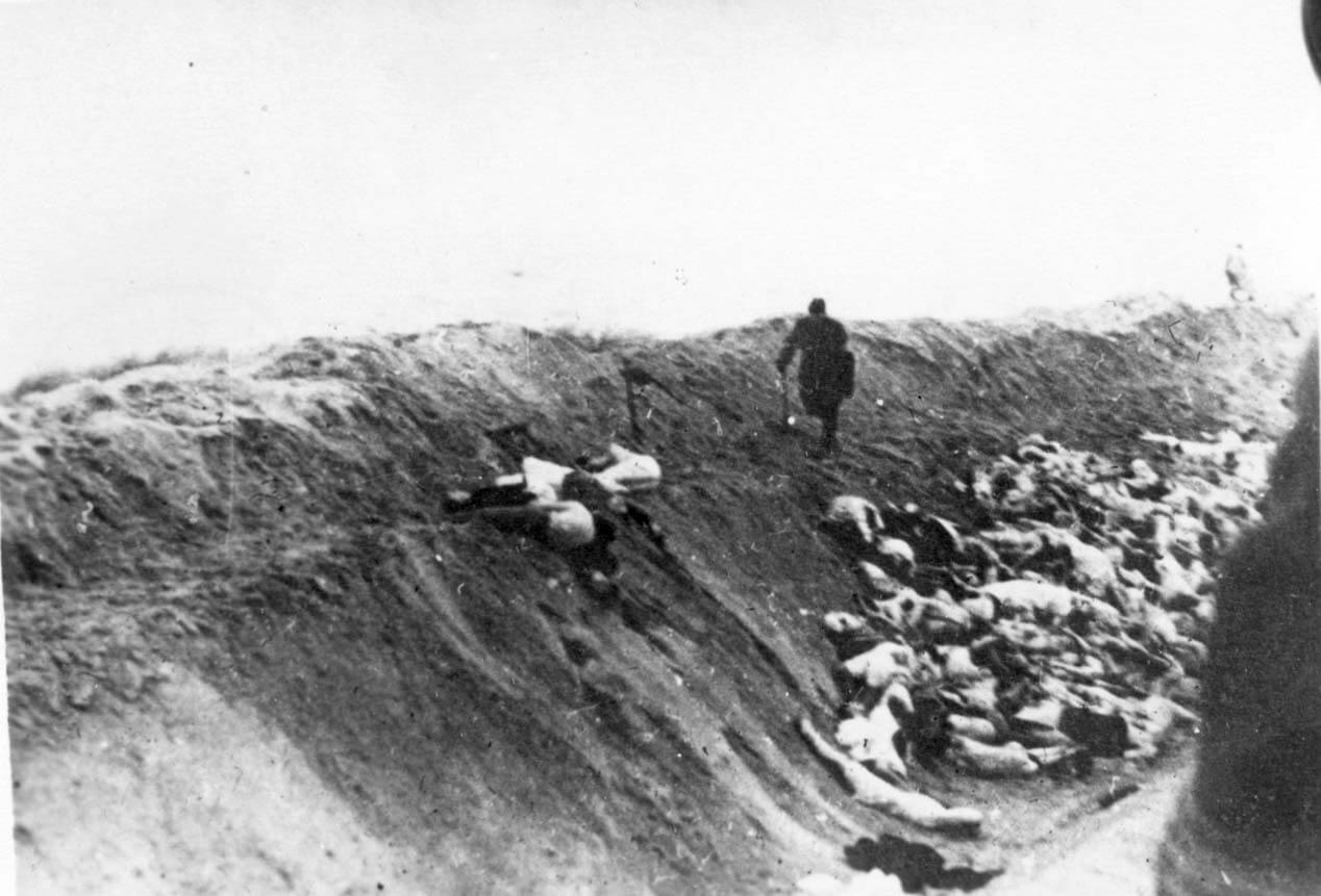 A Latvian collaborator kicks the bodies of Jewish women and children into a ditch after their execution, December 15, 1942 (Yad Vashem). 