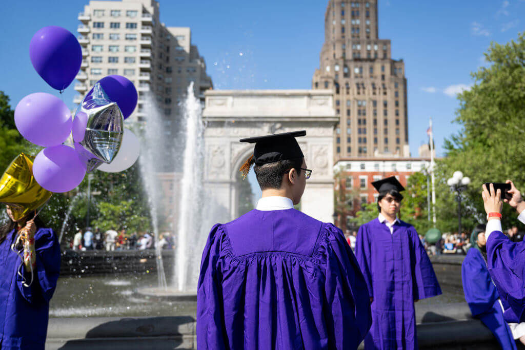  New York University (NYU) graduates take photos wearing caps and gowns in Washington Square Park on May 17, 2022.