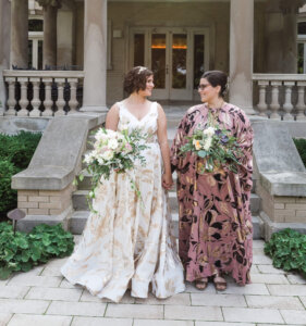 Two women, one in a white wedding gown, the other in a pink patterned gown