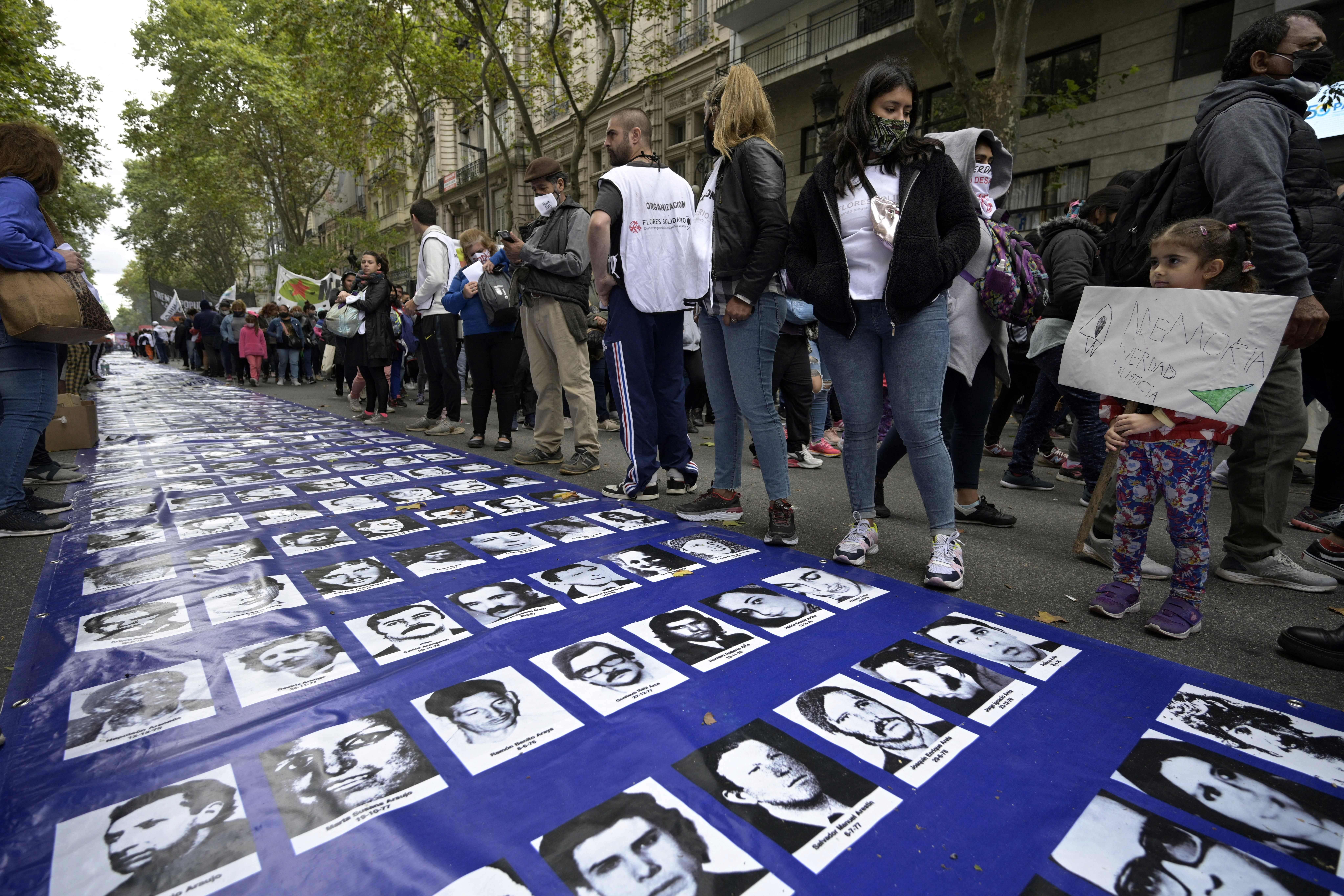A girl holds a banner reading “Memory, Truth, Justice” next to a large banner with portraits of people disappeared during the military dictatorship (1976-1983), at a gathering to commemorate the 46th anniversary of the coup, at Plaza de Mayo Square in Buenos Aires.