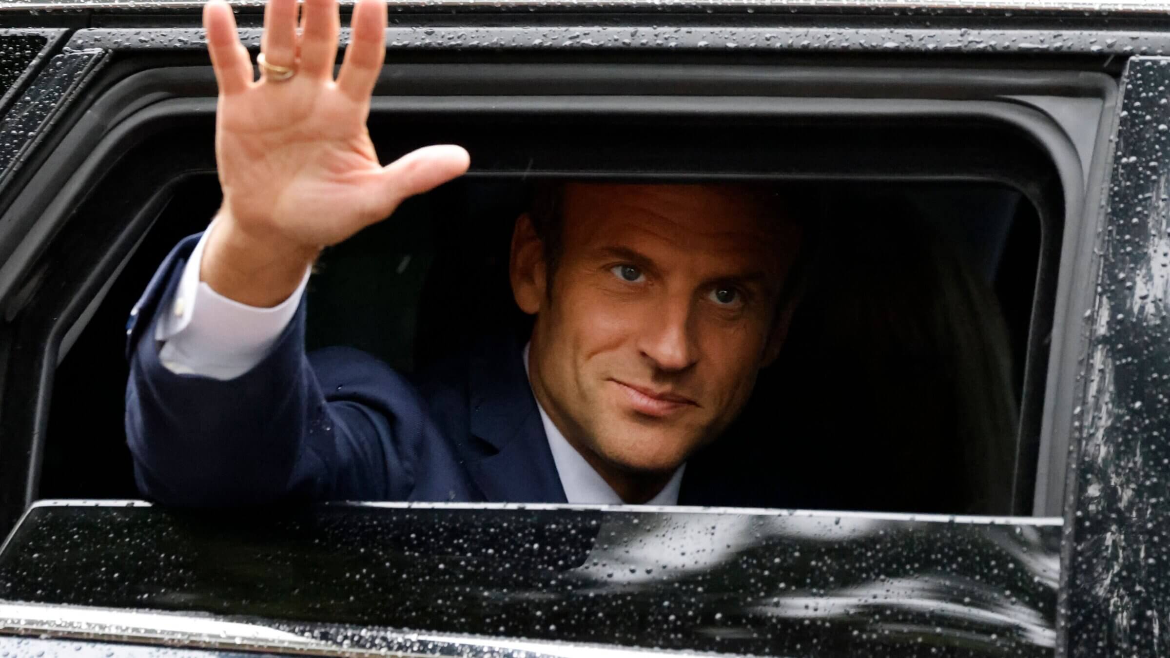 Emmanuel Macron salue depuis la fenêtre d'une voiture.