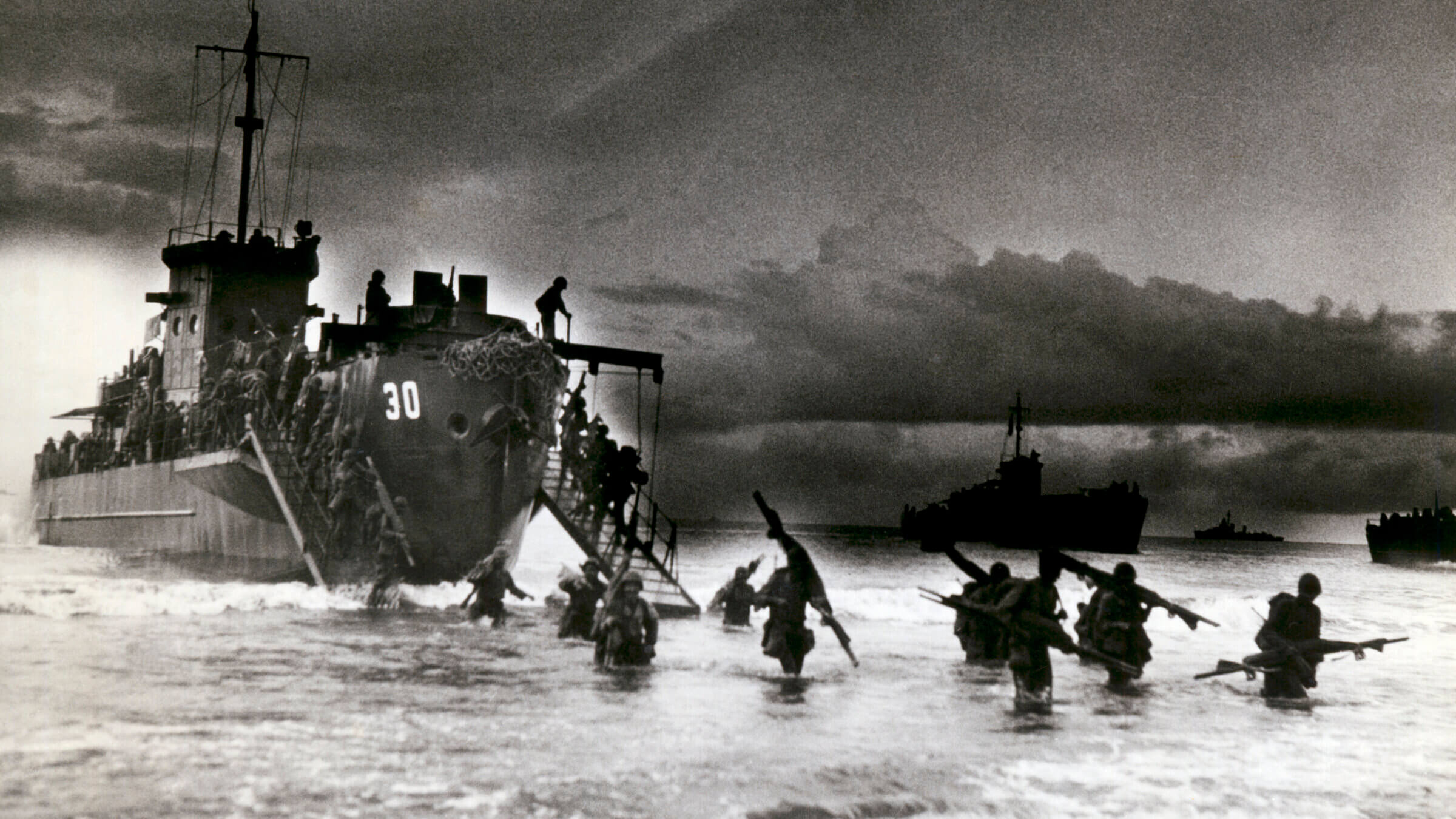 View of Allied troops from a transport vessel, among them medics with stretchers over their shoulders, as they wade ashore during the invasion of Normandy, France, in June 1944.