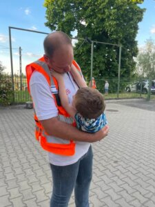 The man in an orange vest holds a little boy in a playful way.
