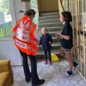 A woman in an orange safety vest interacts with children in an outdoor stairwell