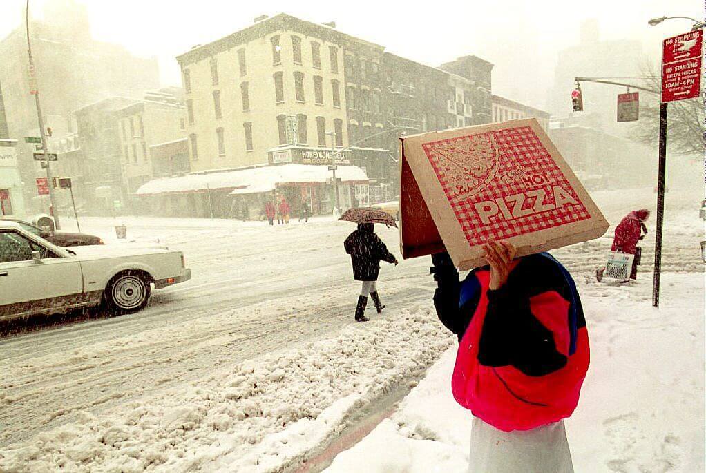 A man holds a pizza box over his head during a snowstorm in New York.