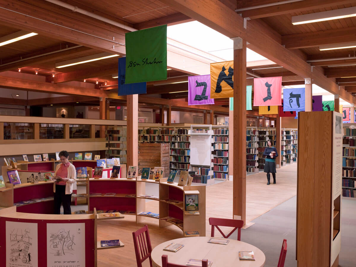 The main library at the Yiddish Book Center features rows of bookshelves with colorful Yiddish letters hanging from banners on the ceiling.