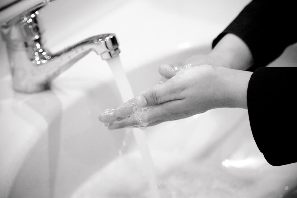 A black and white image of hands washing in a sink. 