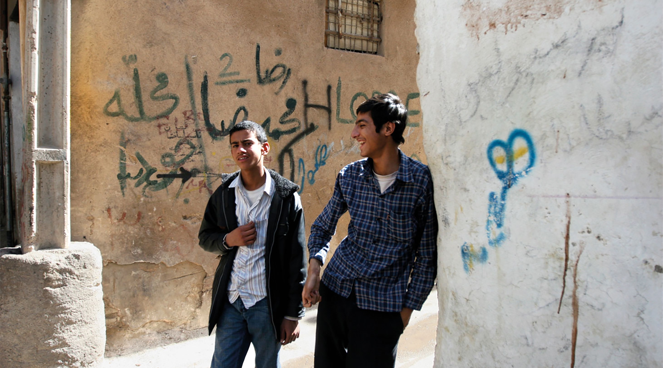Two young men walk in a Jewish neighborhood in Shiraz, Iran. On the wall behind them, a derogatory term for Jews is written in graffiti. (Hassan Sarbakhsian)