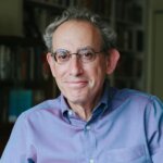 A photograph of the author Ken Kalfus wearing a blue button-down shirt and glasses.