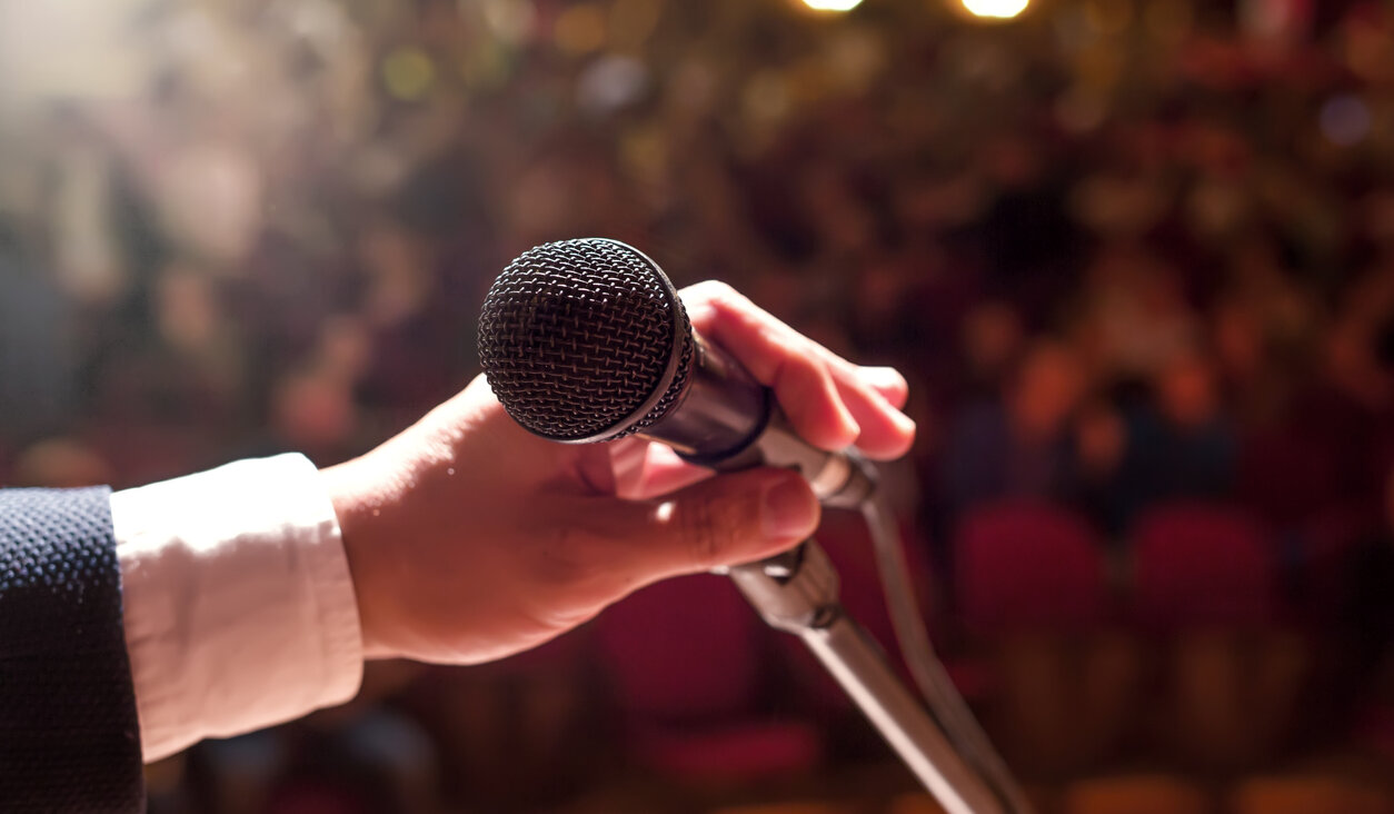 A hand holds a microphone in front of a crowd