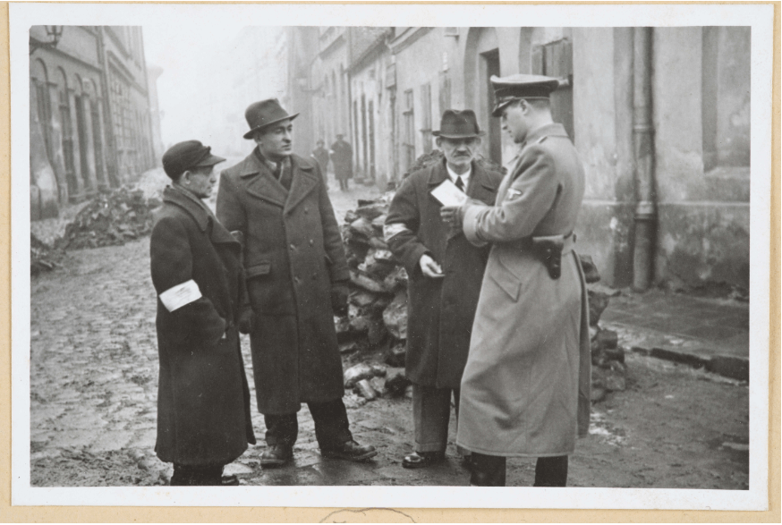 A German policeman checks the identification papers of Jewish people in the Krakow ghetto, Poland, 1941