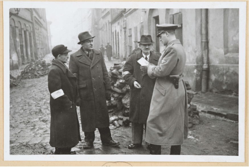 A German policeman checks the identification papers of Jews in the Krakow ghetto. (National Archives in Krakow)