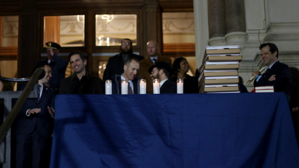 Five candles are lit on a table with people standing behind it