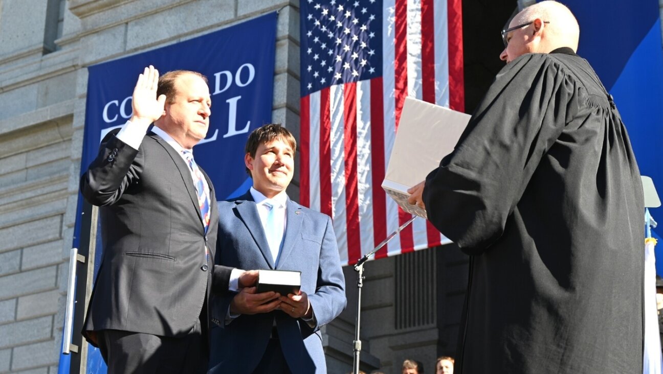 Brian Boatright, the chief justice of the Colorado Supreme Court, at right, swears in Gov. Jared Polis, on the left, while Polis’s husband, Marlon Reis, holds a Hebrew bible, in Denver, Jan. 10, 2023.
