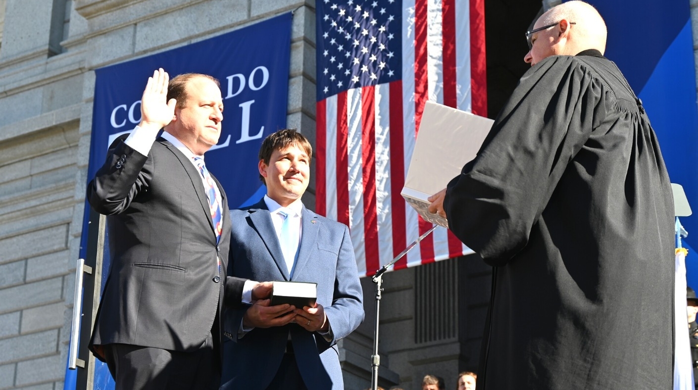 Brian Boatright, the chief justice of the Colorado Supreme Court, at right, swears in Gov. Jared Polis, on the left, while Polis’s husband, Marlon Reis, holds a Hebrew bible, in Denver, Jan. 10, 2023.