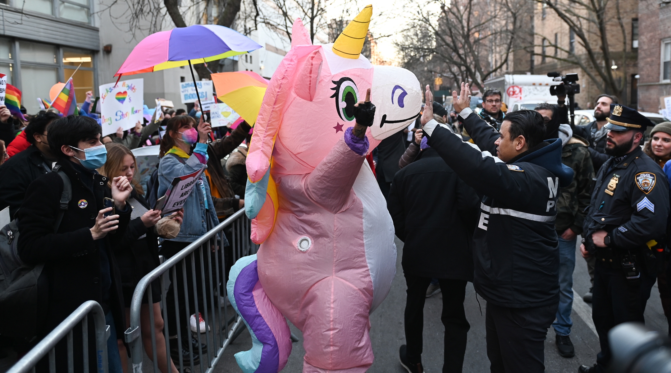 A person dressed in a blow-up unicorn costume stands between the NYPD and defenders of Drag Story Hour at a library in Jackson Heights, Queens last Thursday. (Gili Getz/Courtesy)