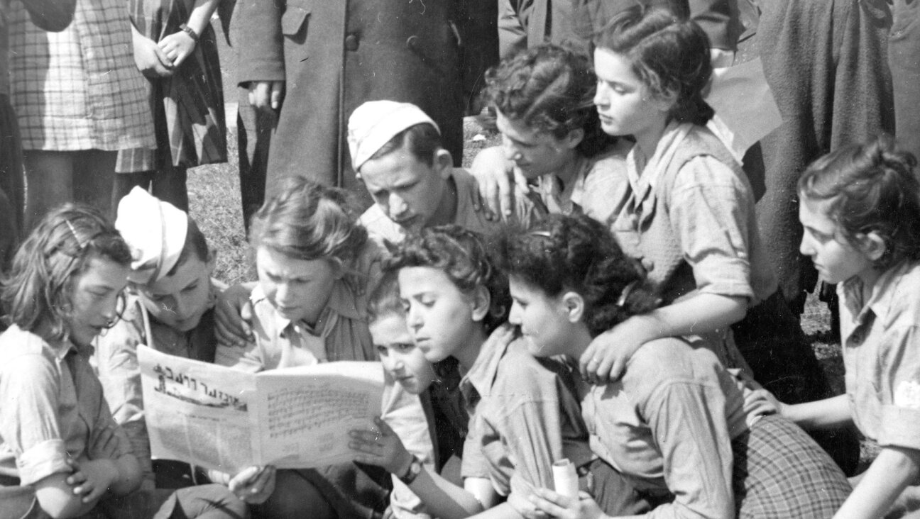A group of children from the Jaeger Kaserne DP camp in Germany read a Yiddish newspaper in an undated photo. (UN Archives)