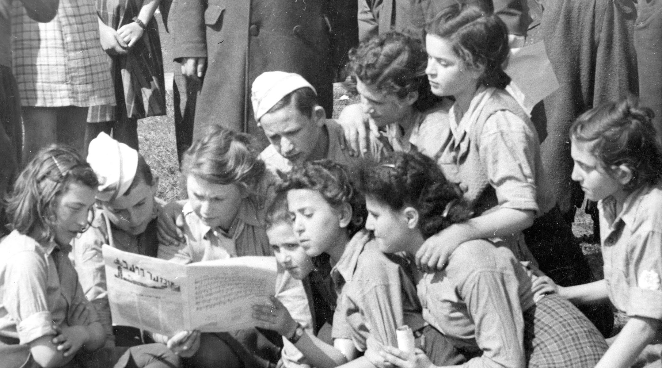 A group of children from the Jaeger Kaserne DP camp in Germany read a Yiddish newspaper in an undated photo. (UN Archives)