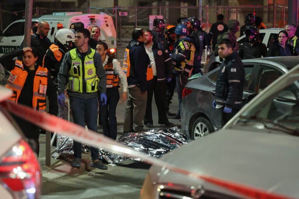 Israeli emergency service personnel and security forces stand near a covered body at the site of a reported attack in a settler neighborhood of East Jerusalem, on Jan. 27, 2023. 