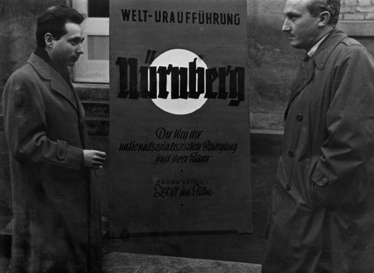 Stuart Schulberg, left, by a poster of his 1948 film <i>Nuremberg: Its Lesson for Today,</i> which premiered in Stuttgart, Germany, but never had a proper American release in his lifetime.