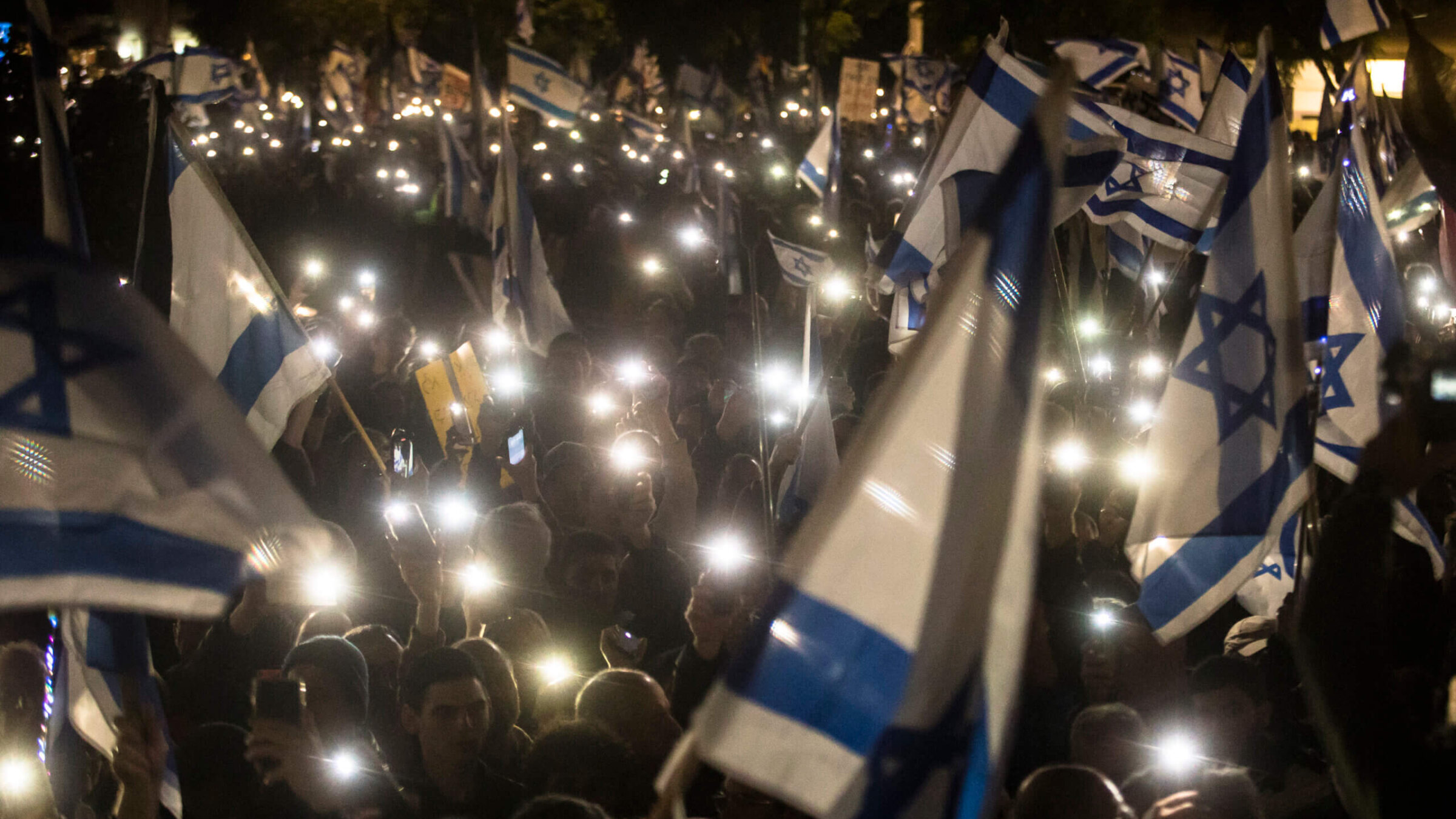 Israelis hold the Israeli flag and light their phones as they protest against the new Israeli far-right government on January 14, 2023 in Tel Aviv, Israel. 