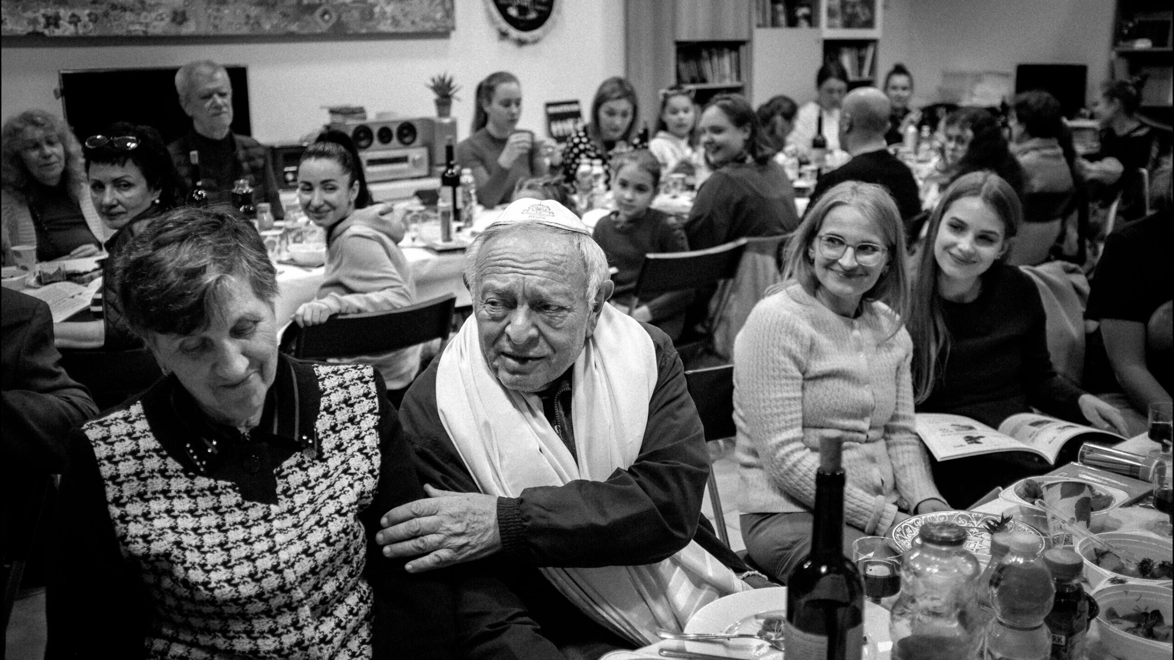 Yaakov Tamarkin, 77, wearing tallit, from Vasylkiv, Ukraine. Next to him is wife of 52 years, Svetlana; on other side is his daughter-in-law, Galina, (glasses) and her daughter. The family is attending a Ukrainian refugee Passover seder at JCC Krakow, April 15, 2022.