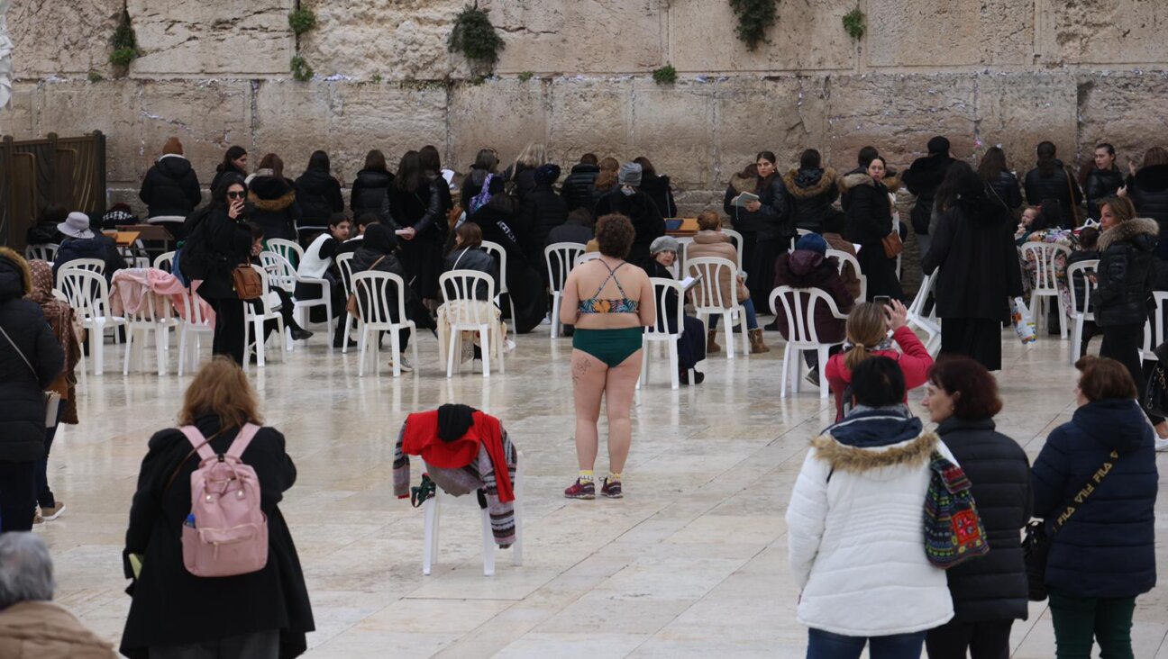 A woman stands in front of the Kotel in Jerusalem, her discarded clothing on the chair behind her.
