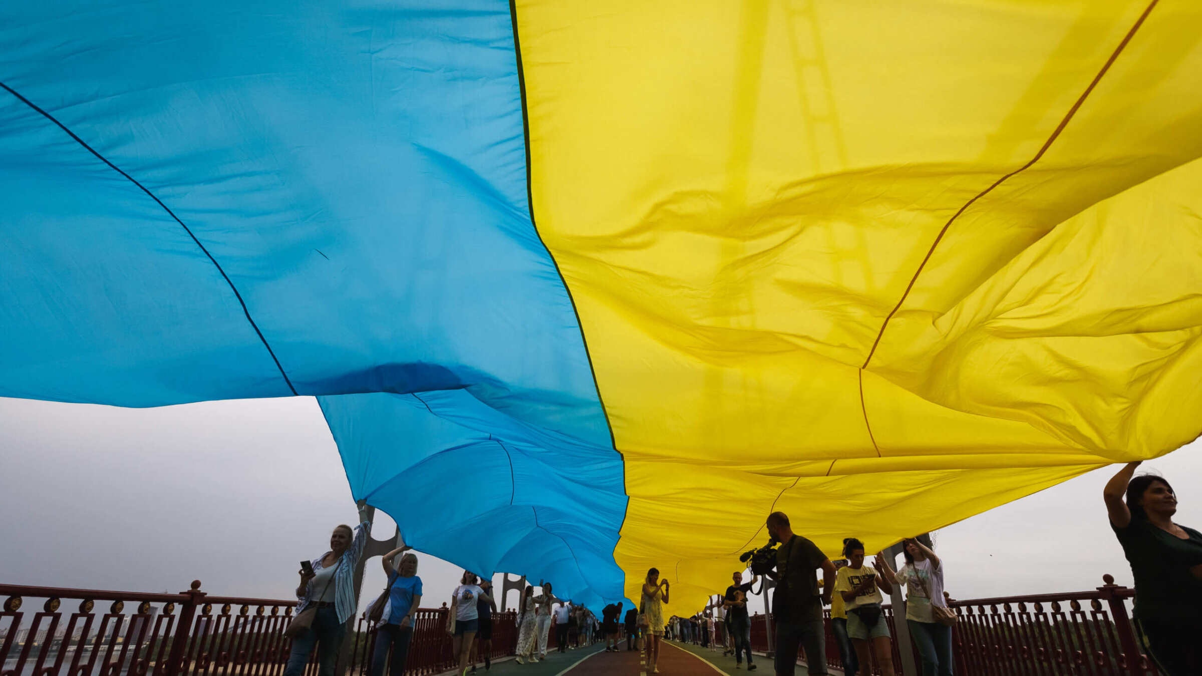 People hold a 430-meter-long Ukrainian flag along the park pedestrian bridge over the Dnipro River during the “Ukraine is united” political performance on August 28, 2022 in Kyiv, Ukraine. The symbolic unification of the left and right banks of the Dnipro demonstrates the unity of the Ukrainian people in the struggle for Ukraine’s independence. 