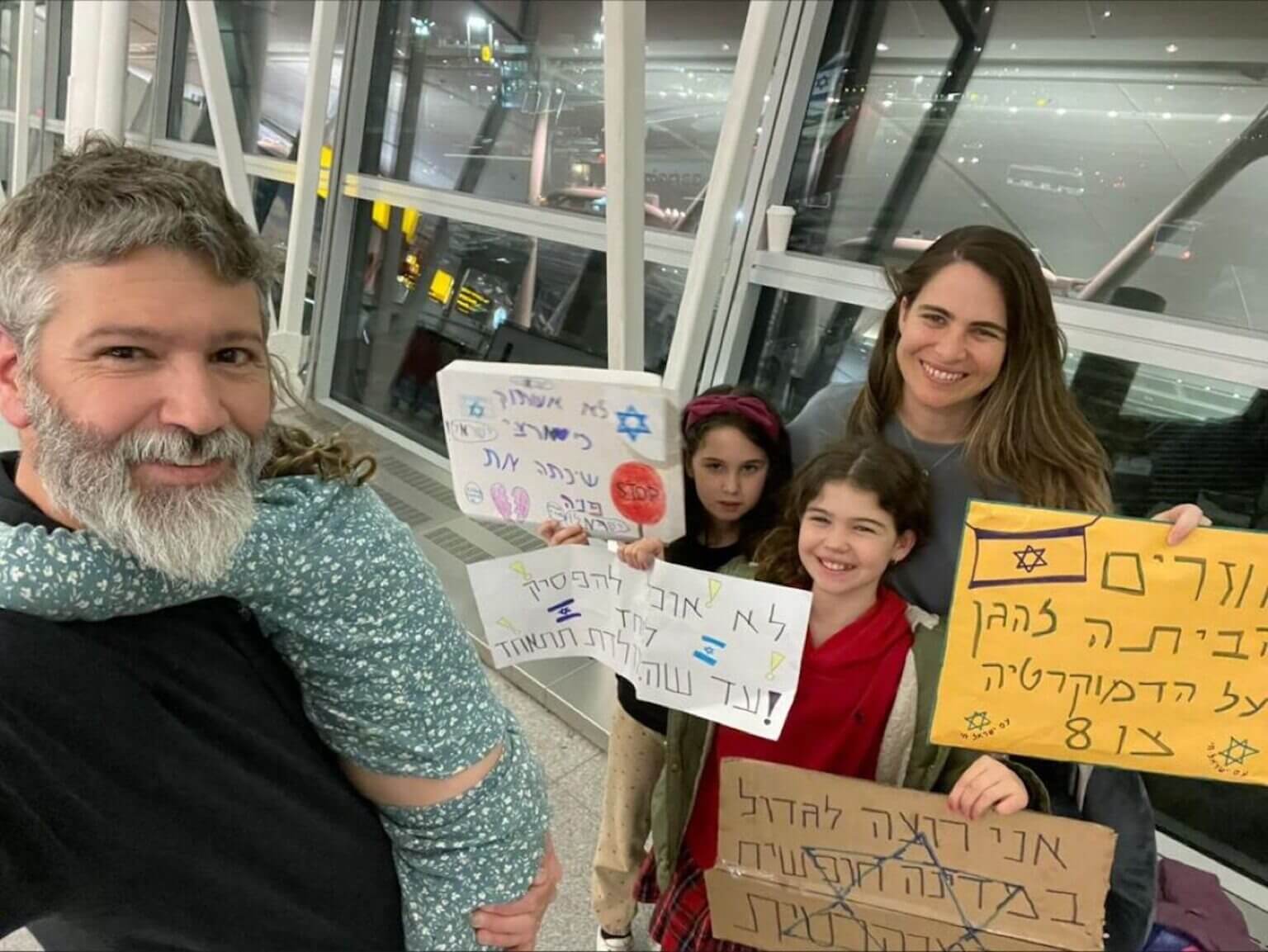 The Breakstone Roth family poses with protest signs in New York City’s John F. Kennedy International Airport en route to Israel, March 27, 2023. 