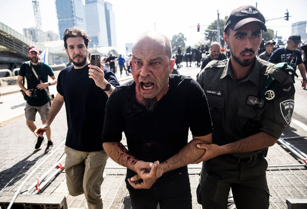 A man injured in clashes at an anti-government demonstration in Tel Aviv on Wednesday is led away by police. 