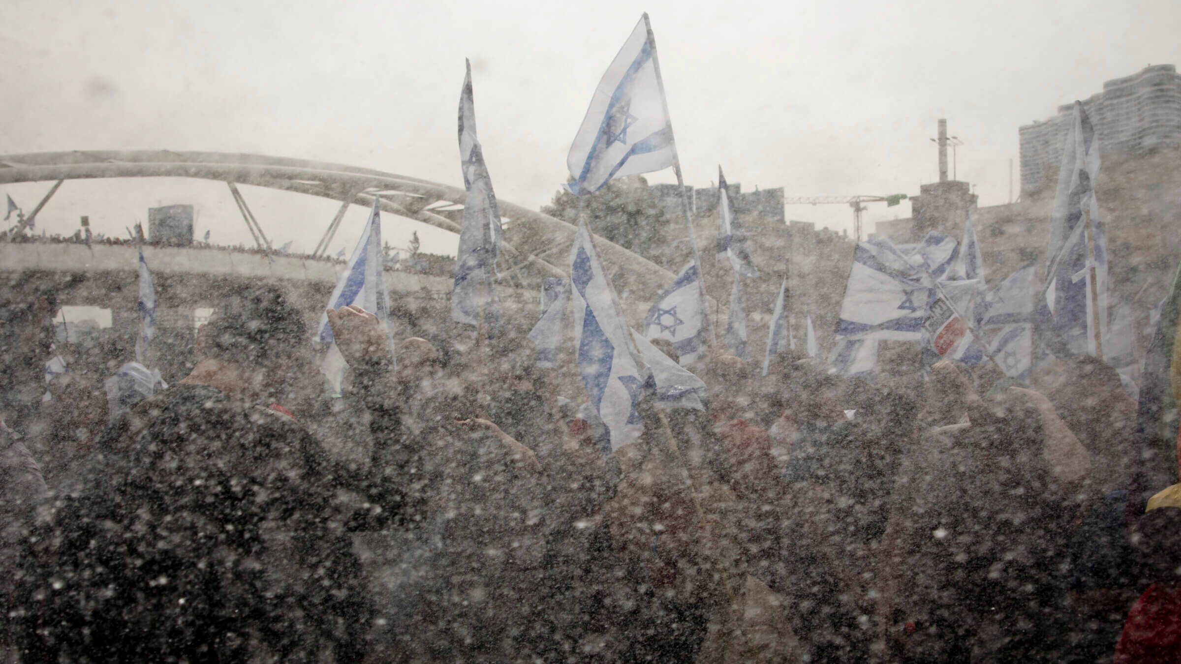 Israeli protesters hold the Israeli flag as Israeli police use a water cannon to evacuate protesters from a main highway during a rally against the Israeli government's judiciary overhaul on March 23, 2023 in Tel Aviv, Israel