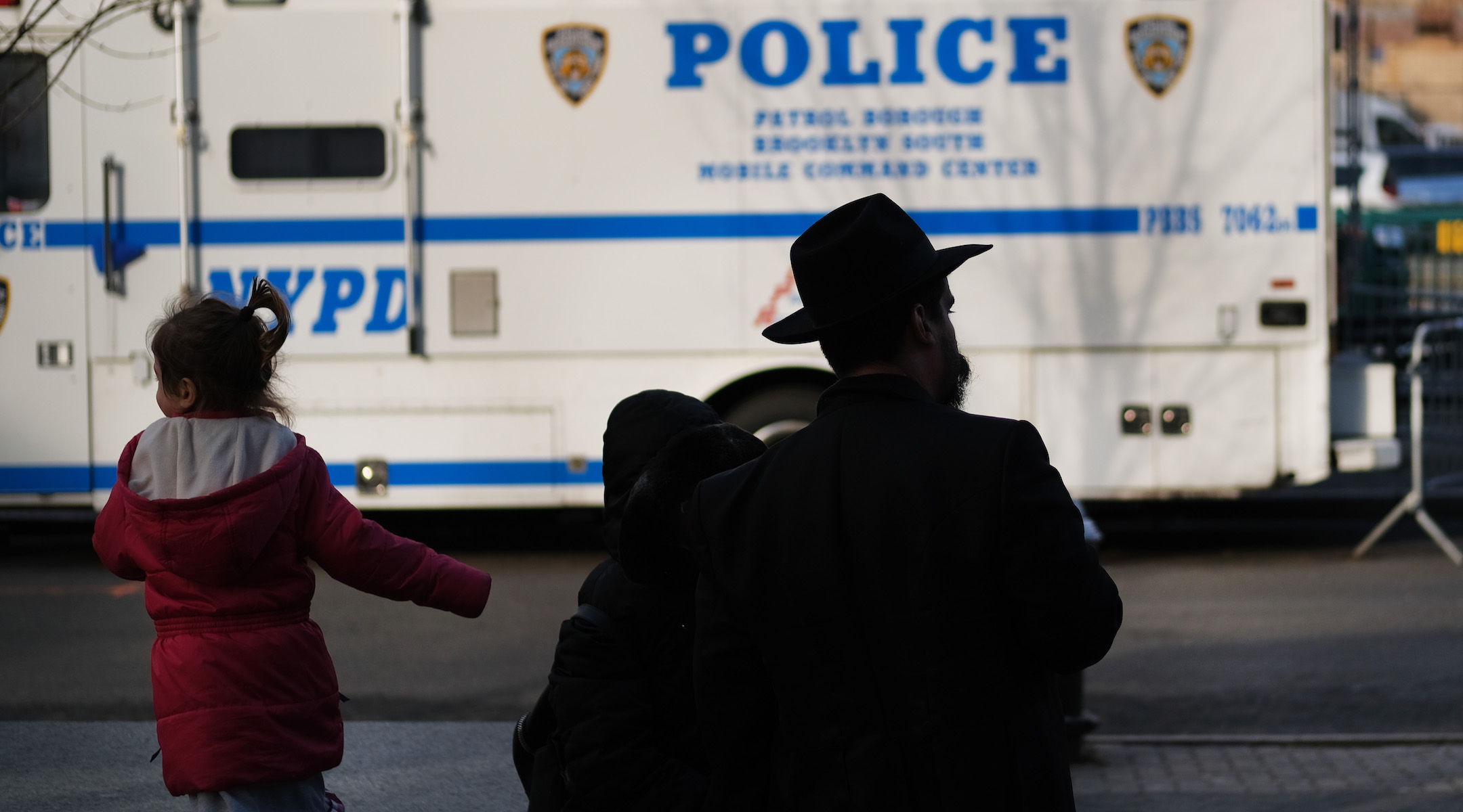 A man and girl in the Crown Heights neighborhood of Brooklyn stand opposite a police van, Dec. 31, 2019. Brooklyn was the location of more than one-third of the total number of anti-Semitic assaults committed last year, according to the Anti-Defamation League. (Spencer Platt/Getty Images)