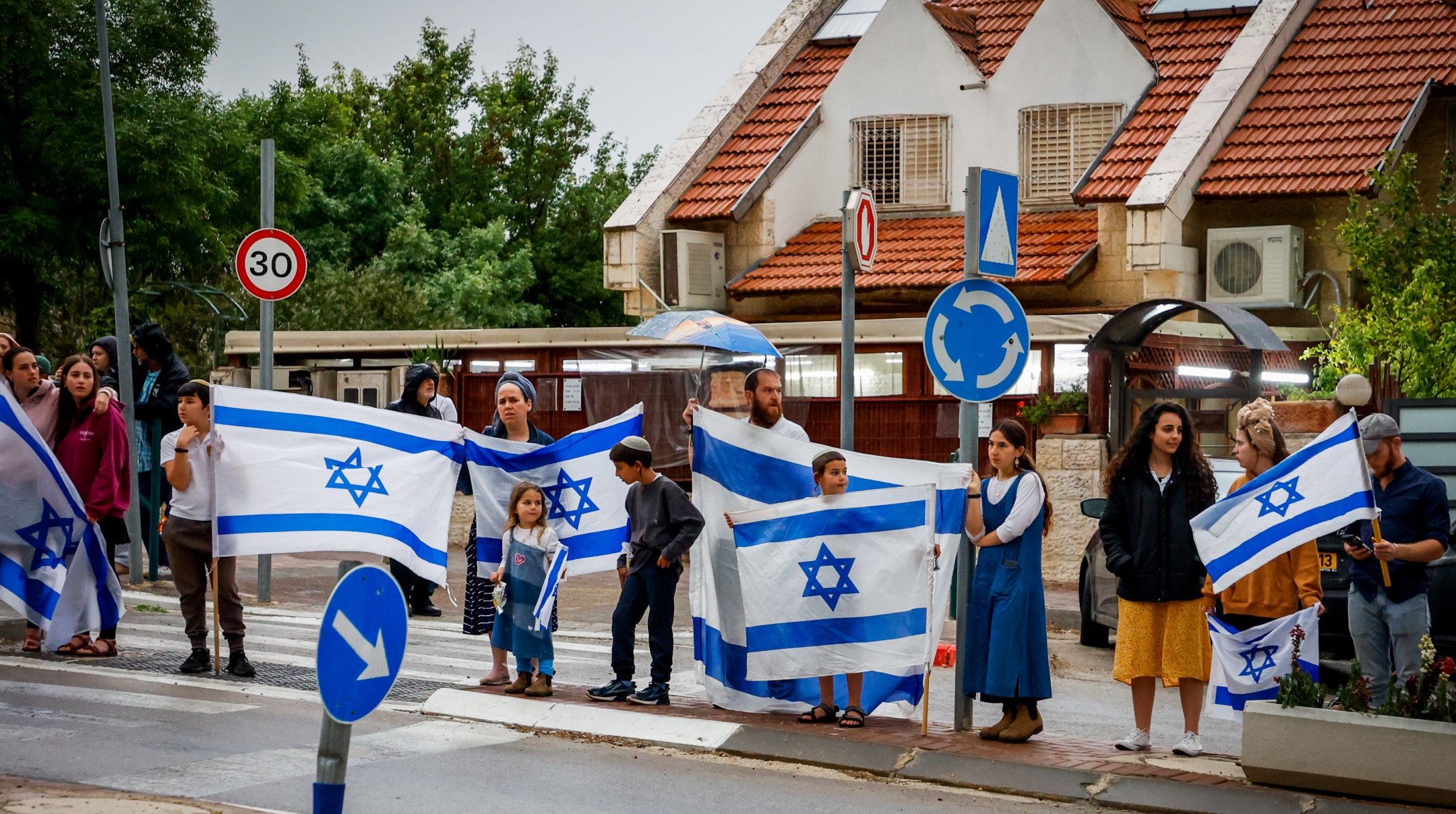 Efrat Residents standing outside their homes with Israeli flags to show solidarity with the Dee family, following the death of Lucy Dee, who died of her wounds three days after the deadly terror attack that killed her two daughters Rina and Maia, in Efrat, in the West Bank, April 10, 2023. (Gershon Elinson/Flash90)