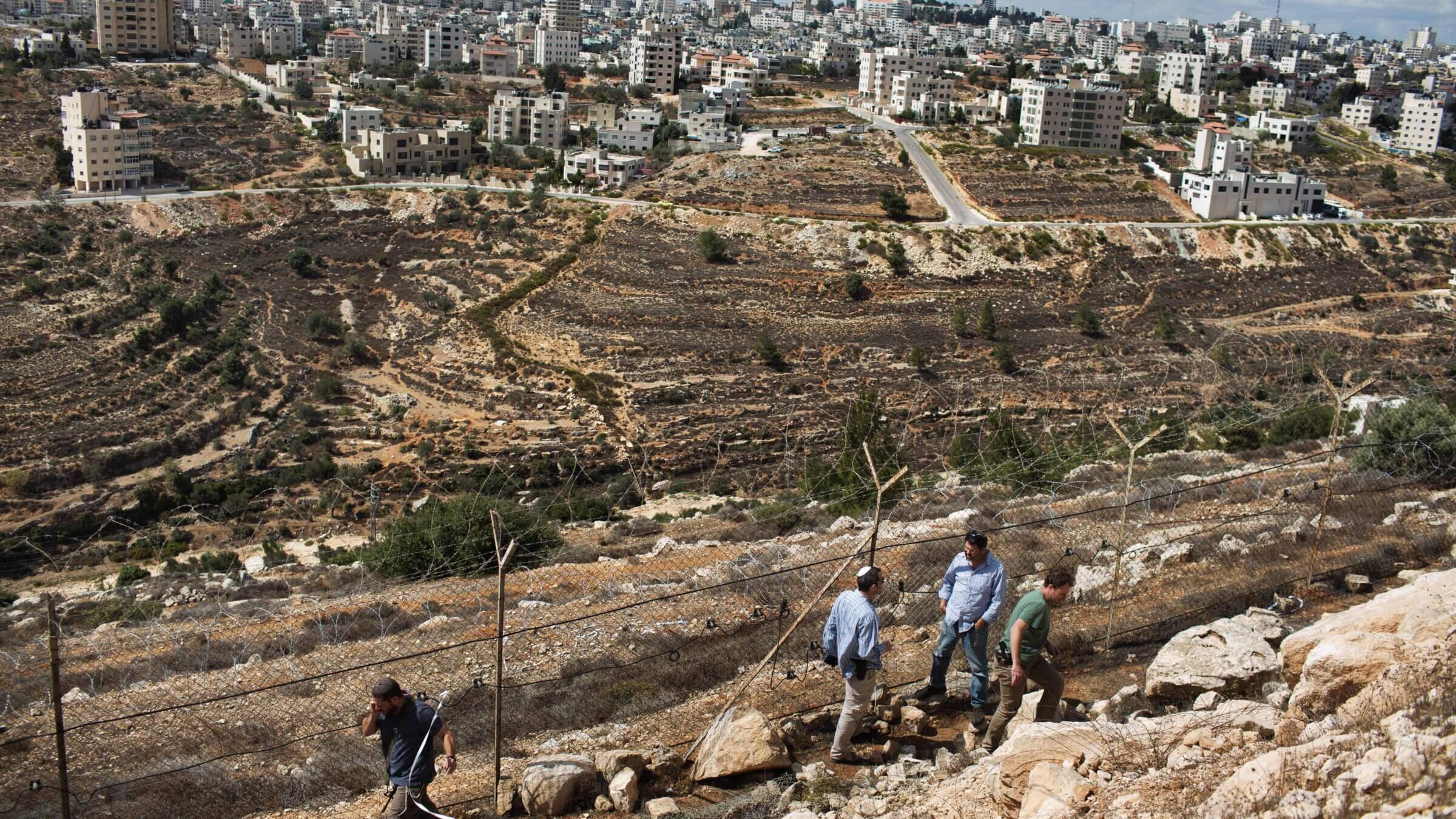 Armed Israeli settlers walk next to the fence between the Jewish settlement of Psagot and the Palestinian town of Al-Bireh in 2013. The Jewish Federations of North America and UJA-Federation sponsored a conference promoting Israel economic development in the West Bank.