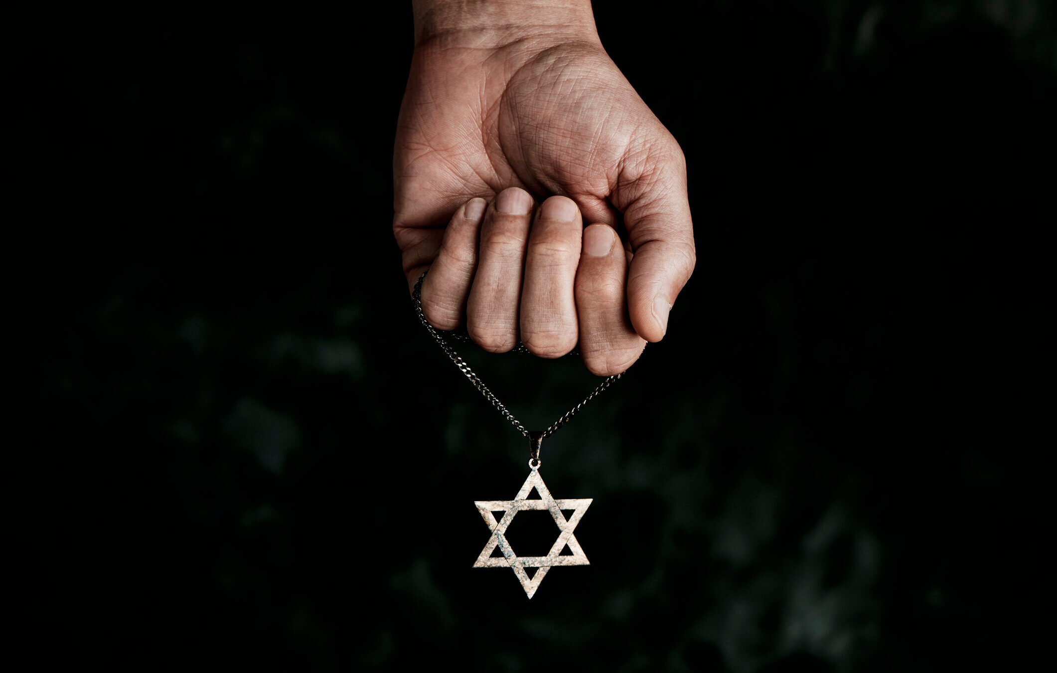 A hand holds a Star of David necklace