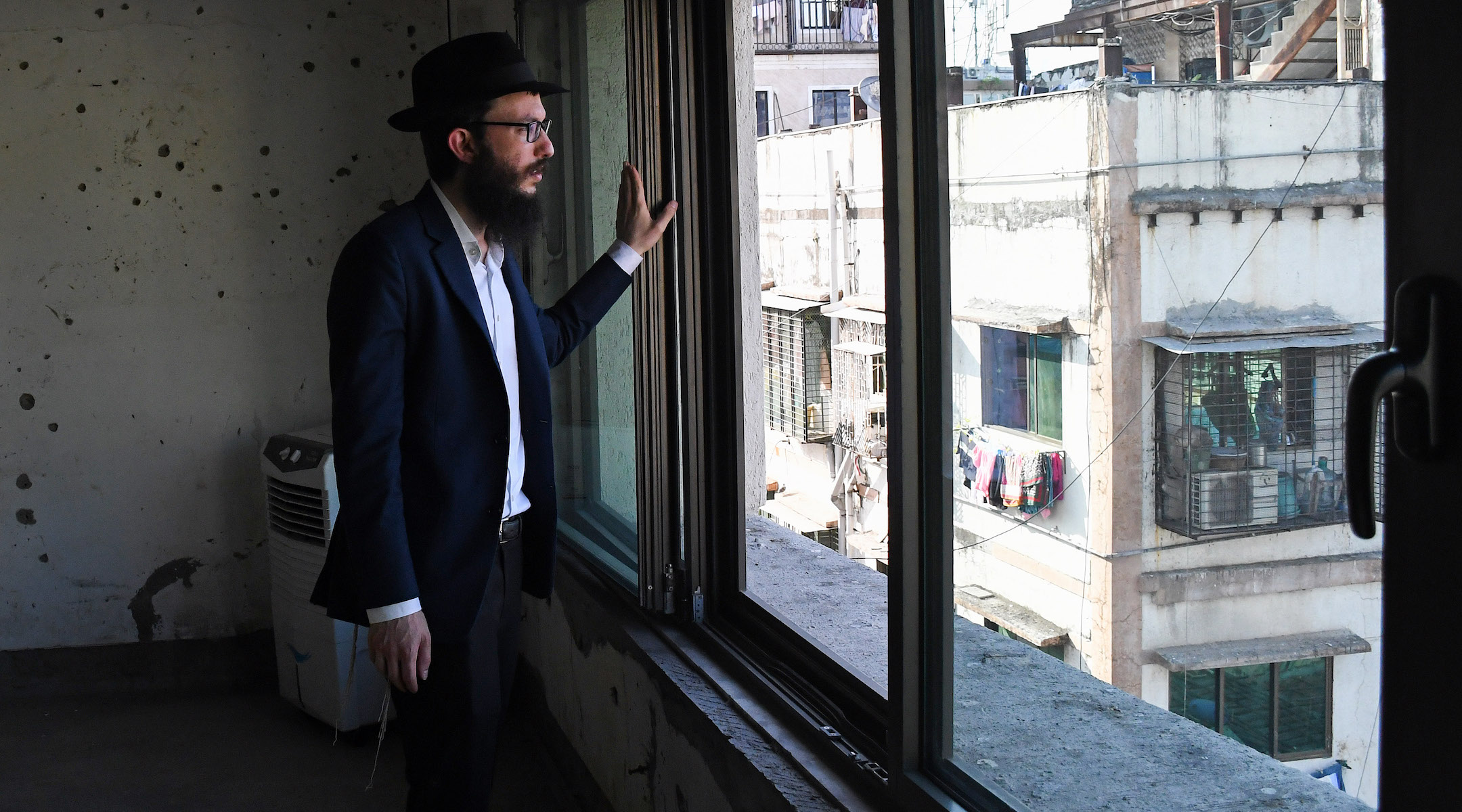 Rabbi Israel Kozlovsky, director of Mumbai’s Chabad center, looks out of a window of the center, in front of a wall pock-marked with bullet holes from the 2008 terror attack. (Ashish Vaishnav/SOPA Images/LightRocket via Getty Images)