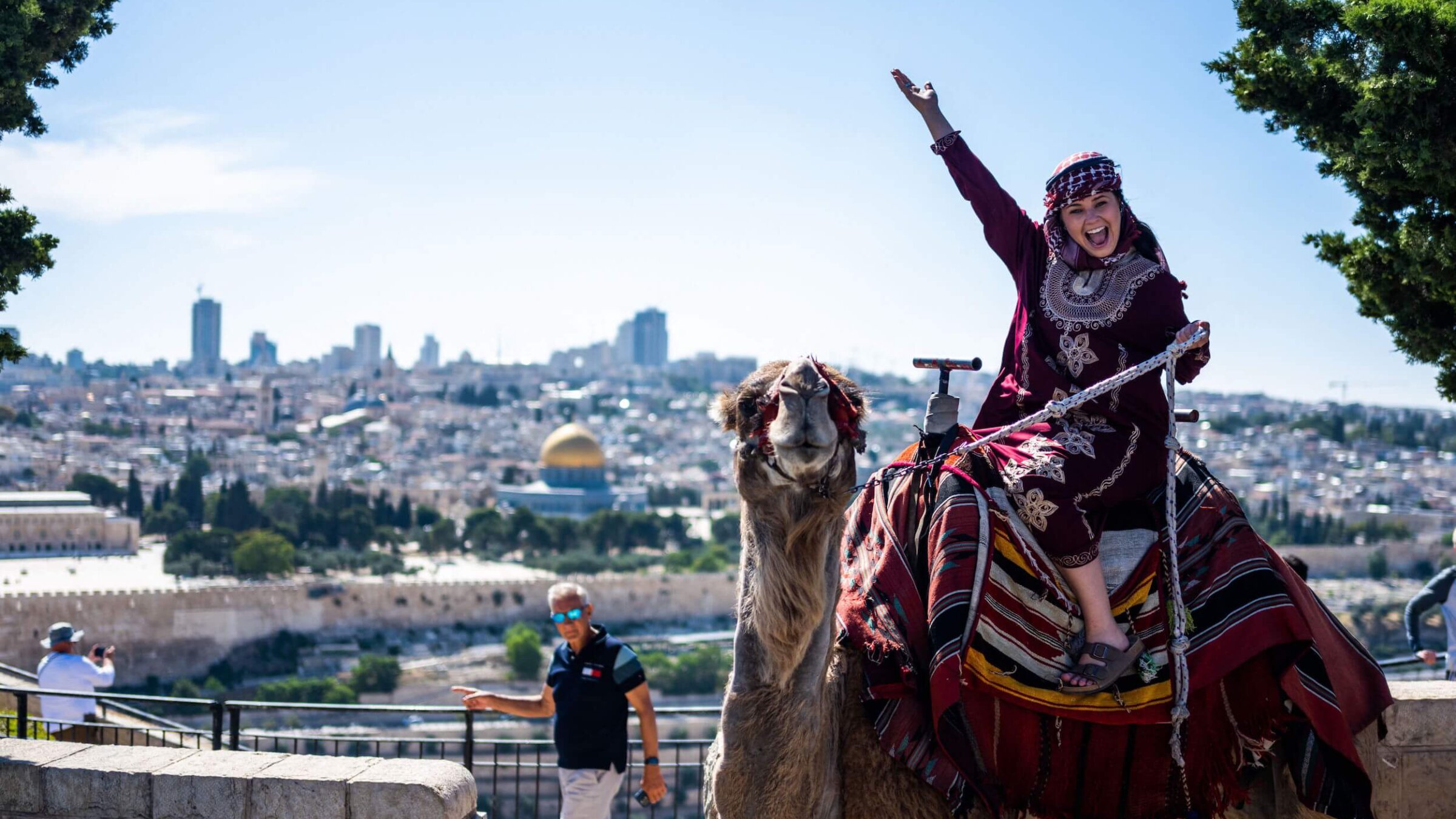 A tourist poses for photos while riding a camel on the Mount of Olives overlooking the old city of Jerusalem on June 12, 2023. 