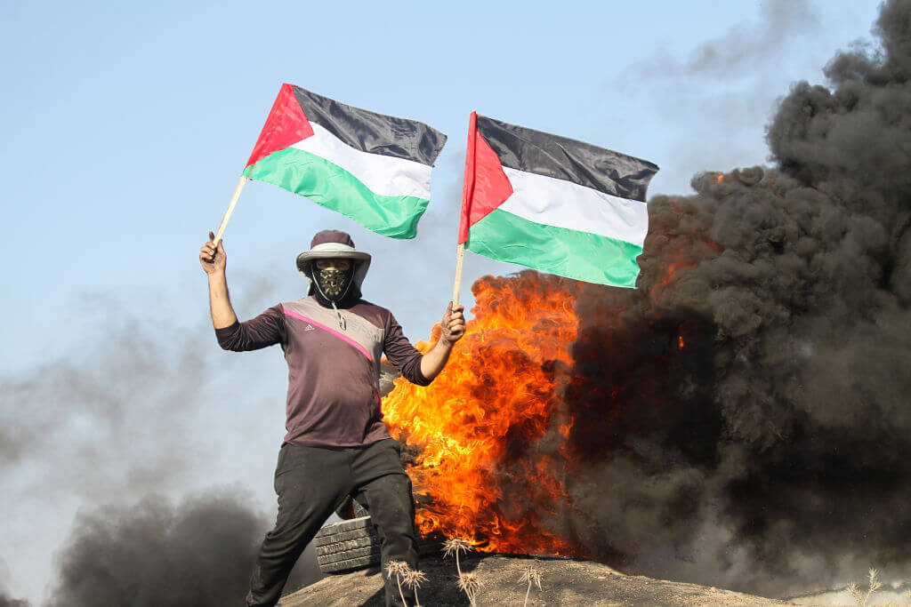 Palestinians burn tires and wave the national flag in protest against the incursion into Jenin on July 3, 2023 along the border fence with Israel, east of Gaza City. 