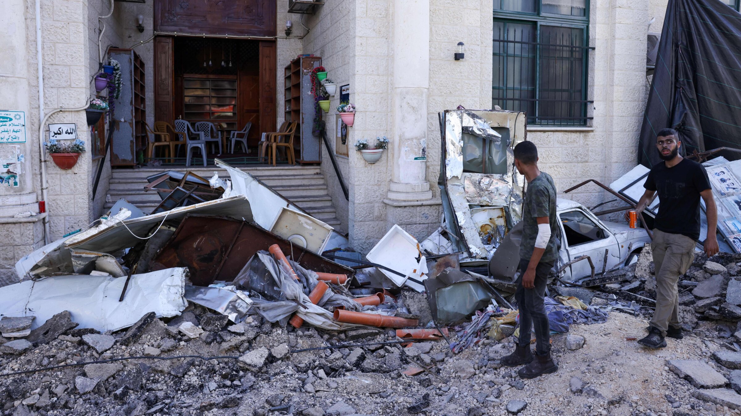 Men walk among rubble in front of a building in the occupied West Bank city of Jenin on July 4, 2023.