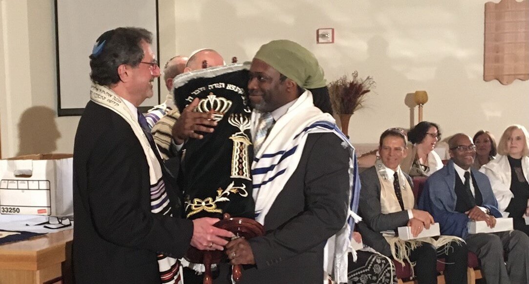 Walter Isaac, holding Torah, is congratulated by Rabbi Monte Sugarman as he becomes the 100th rabbi ordained by the Jewish Spiritual Leadership Institute in 2016