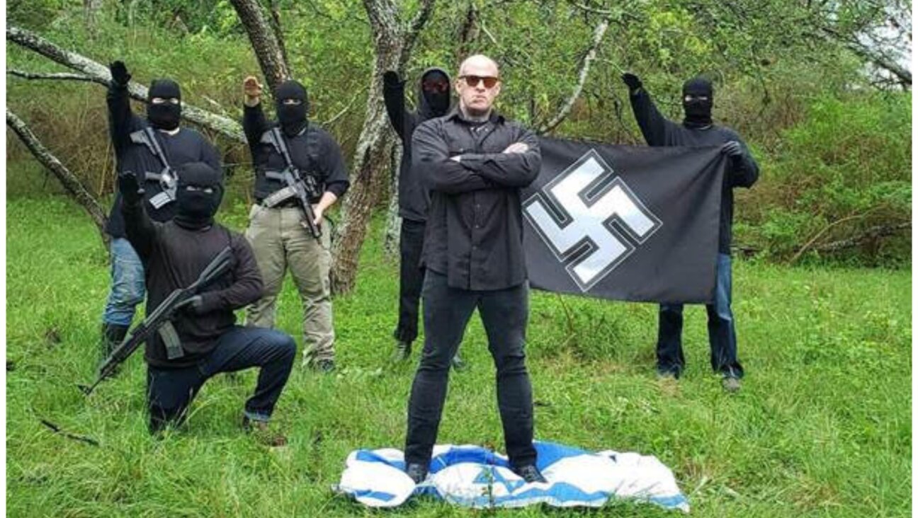 Neo-Nazi Christopher Pohlhaus stands on an Israeli flag while supporters make the Nazi salute and hold a swastika banner. 