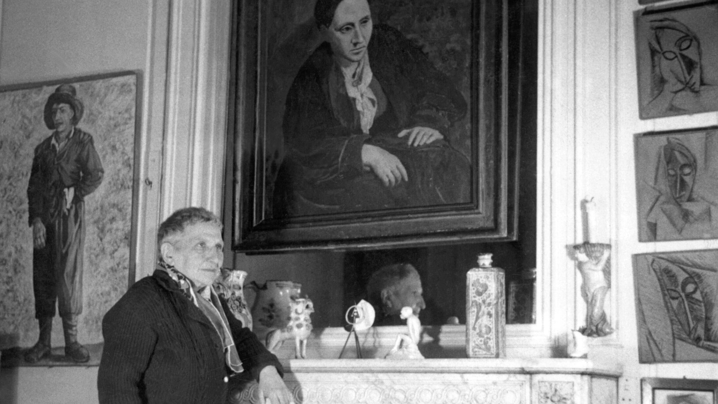 Gertrude Stein poses in front of the portrait of her that Picasso painted in 1906.
