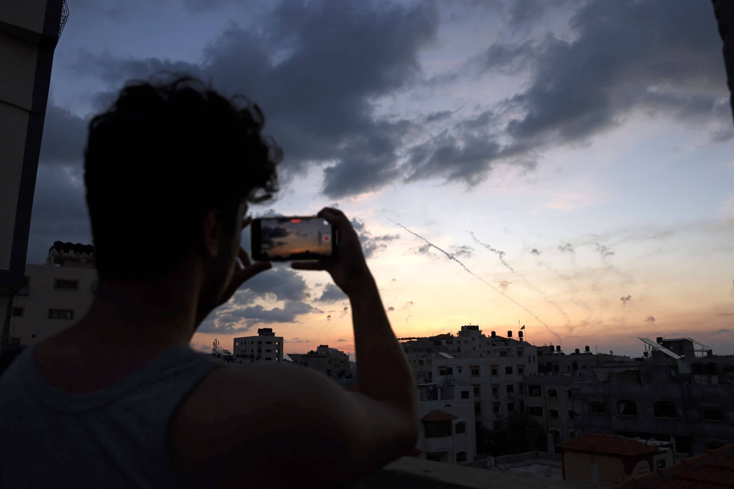 A man records a video with his mobile phone of rockets being fired from Gaza City towards Israel.