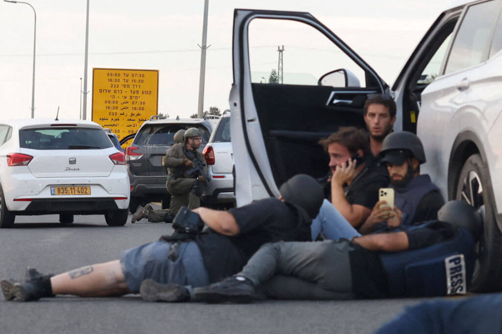 Journalists take cover behind cars as Israeli soldiers take position during clashes with Palestinian fighters near the Gevim Kibbutz, close to the border with Gaza on October 7, 2023. 