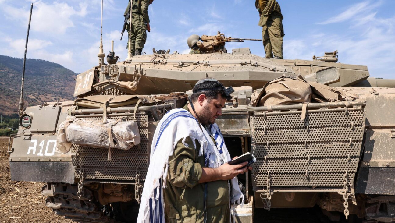 An Israeli solder prays in front of an IDF tank on the outskirts of Kiryat Shmona, a northern town near the border with Lebanon. (JALAA MAREY/AFP via Getty Images)