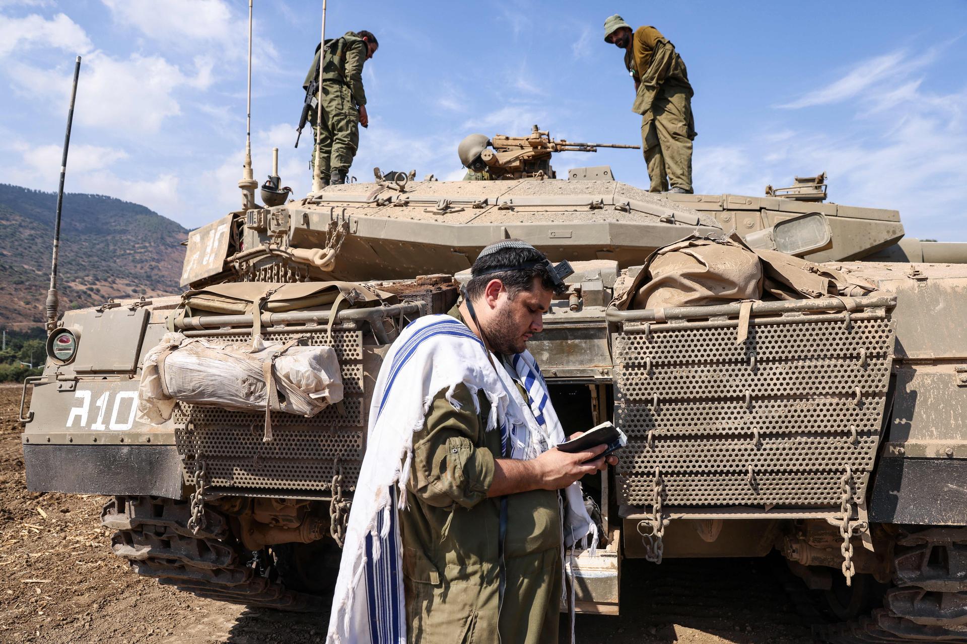 An Israeli solder prays in front of an IDF tank on the outskirts of Kiryat Shmona, a northern town near the border with Lebanon. (JALAA MAREY/AFP via Getty Images)